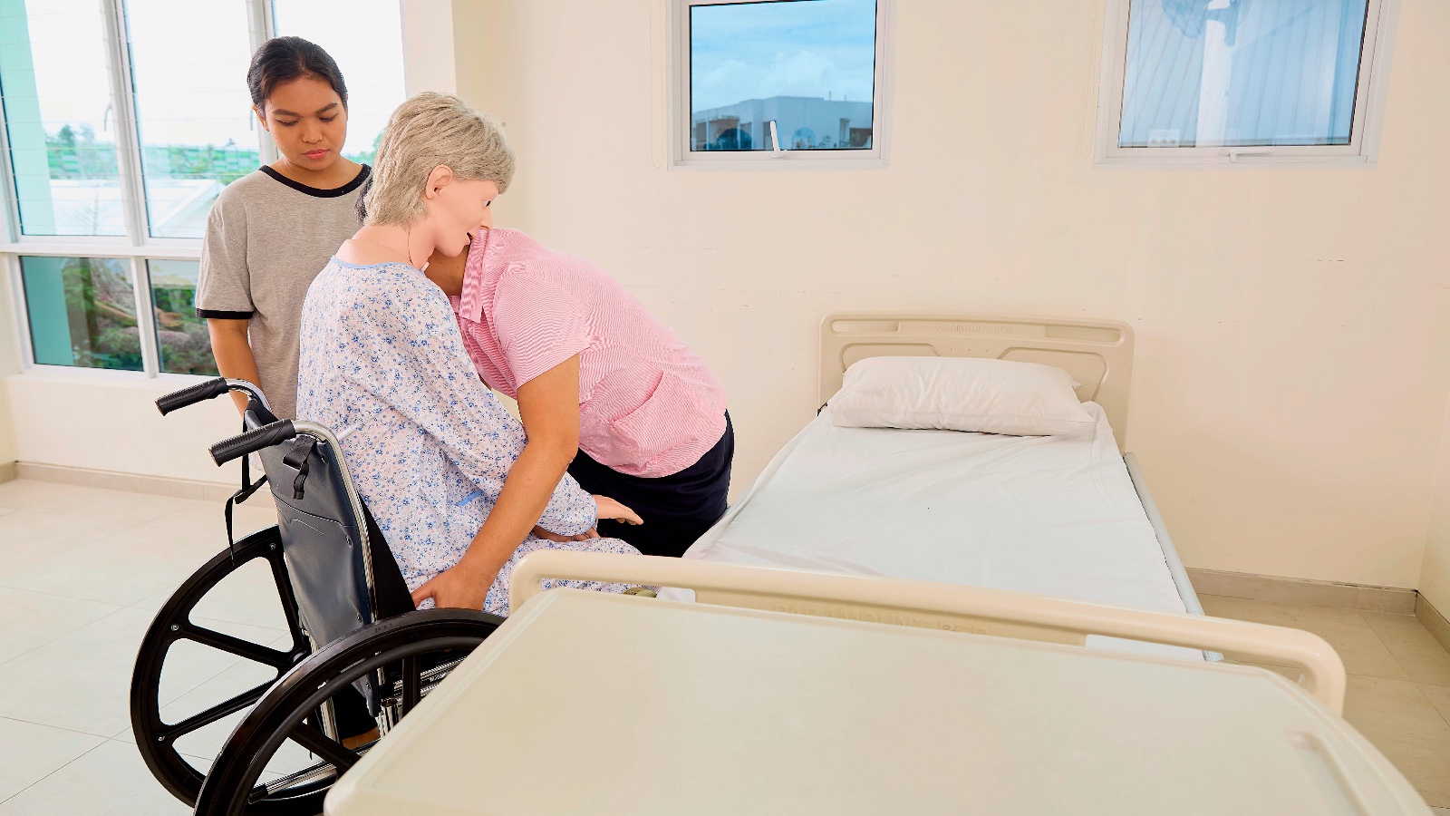 trainer demonstrating final step in transferring an elderly person from bed to wheelchair