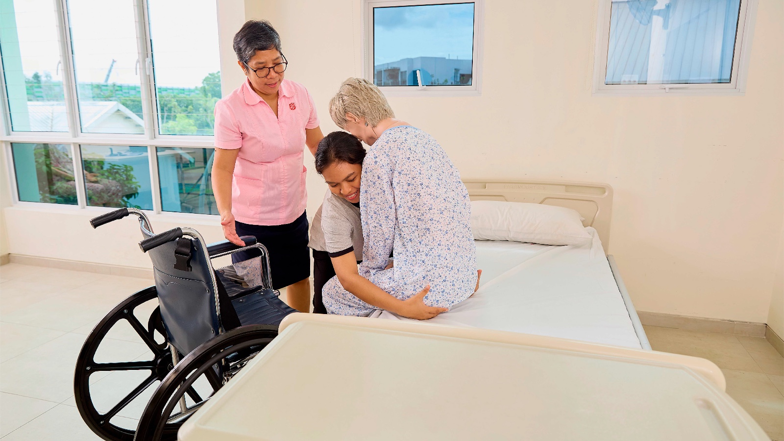 helper practising final step in transferring elderly person from bed to wheelchair